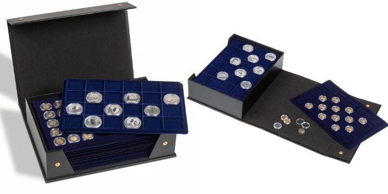 Two open deluxe black coin presentation cases, one showing a stacked dark blue velvet tray with large silver coins and the other displaying individual coins in round capsules, one on an open flat.