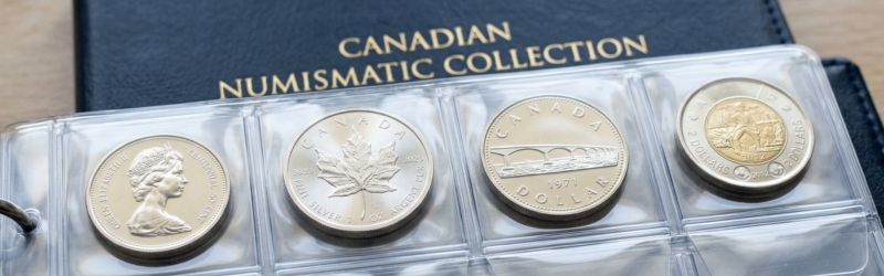A plastic coin collector's sleeve displaying four Canadian coins, including a Silver Maple Leaf and a 50-cent piece, sitting atop a black "Canadian Numismatic Collection" album.