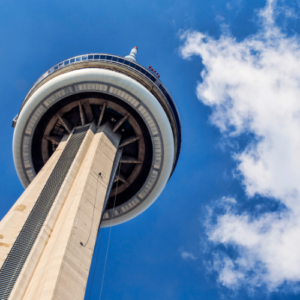 Low-angle view of the CN Tower reaching into a blue sky with white clouds.