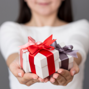 A woman holding out three small beautifully wrapped white gift boxes with colorful satin bows