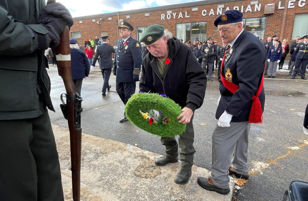 A veteran placing a green remembrance wreath during a memorial service outside a Royal Canadian Legion hall